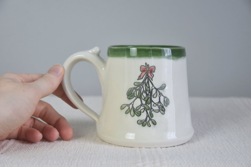 Handmade ceramic Christmas Mug with classic Mistletoe design, red bow, and green rim. 