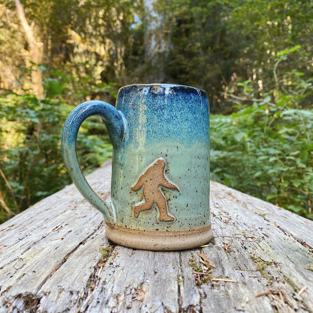 Sasquatch Mug on log in woods . Handmade mug from Winchester, KY